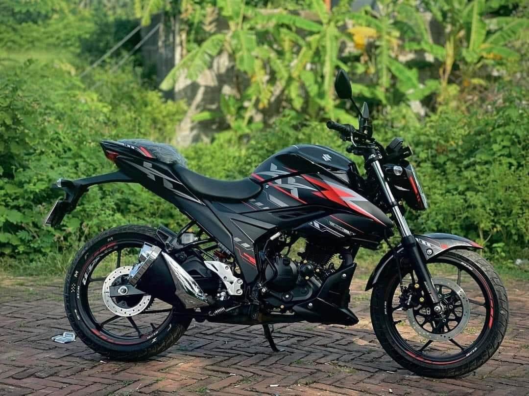 Black Gixxer FI XX motorcycle with a red and black decal set, parked on a brick pathway in front of greenery.
